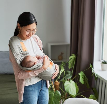 Asian happy mother holding her baby and cradling her while walking around the room